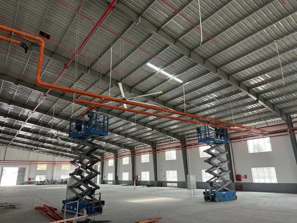 Xe nâng người cắt kéo đang thi công tuyến máng cáp và ống trên cao sát mái nhà xưởng