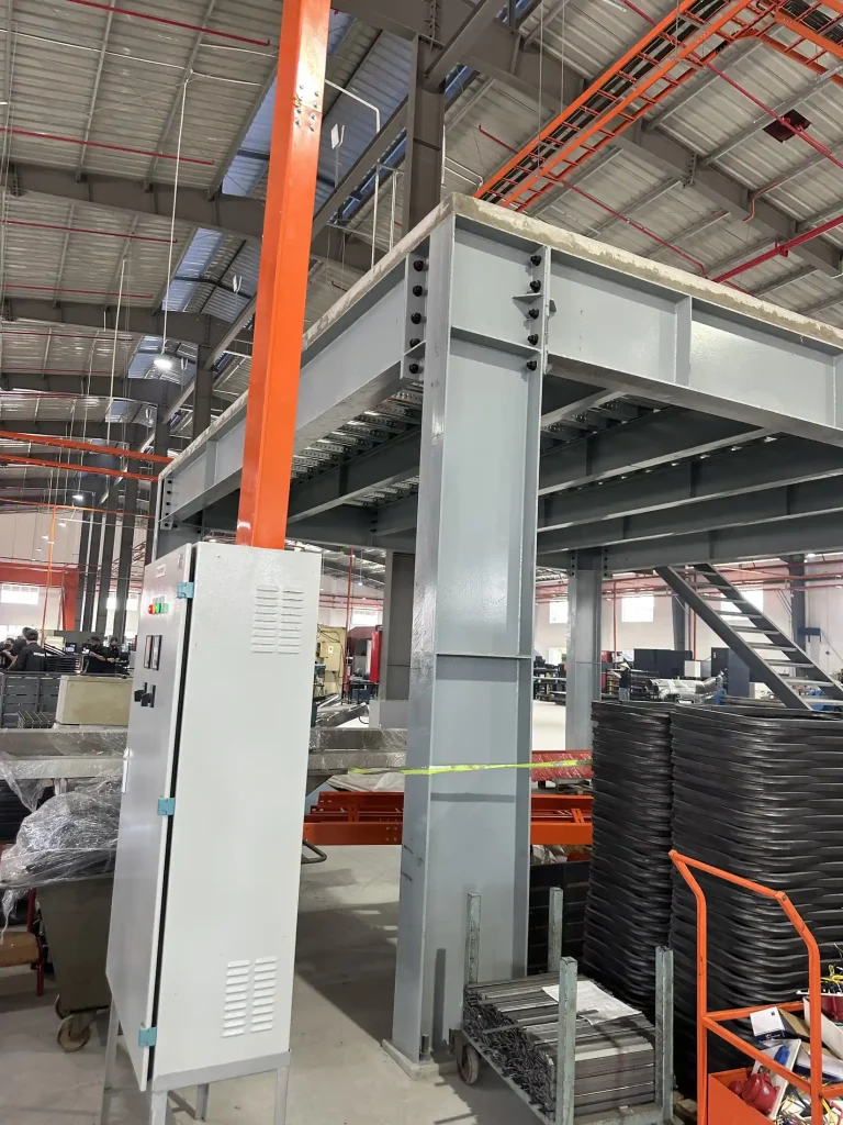 Máng cáp đi đứng dọc cột thép nhà xưởng, bên cạnh tủ điện và ống màu cam